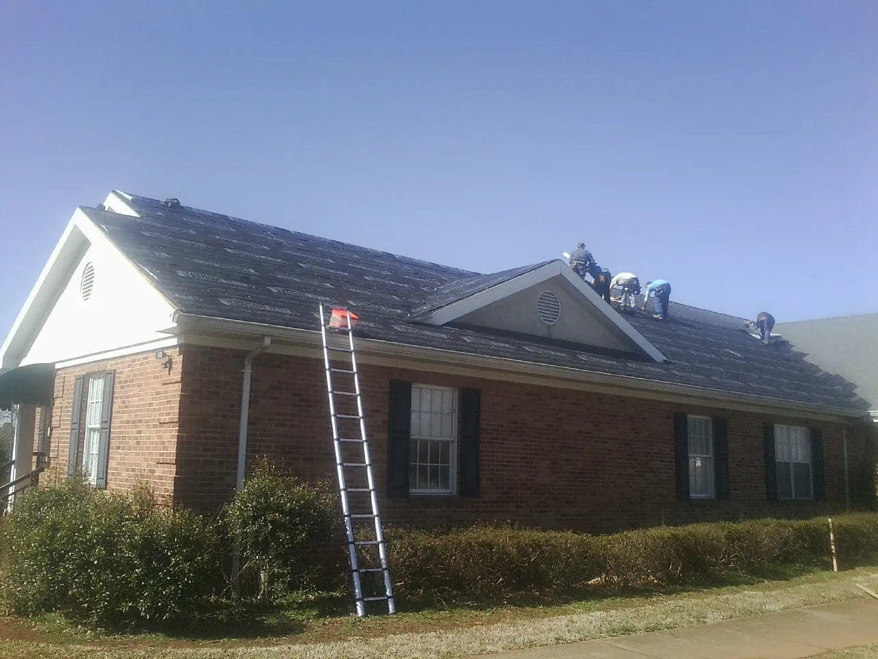 Crew tearing shingles off a brick ranch roof with a ladder set — Metal Roof Repair work by our crew in Ocoee