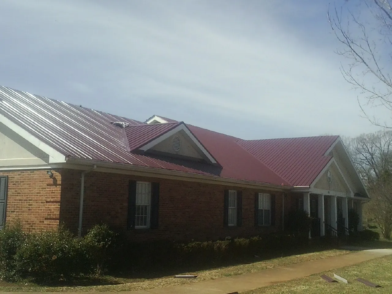 Red metal roof with gabled entries on a long brick building, from a Hail Damage Roof Repair job in Ocoee