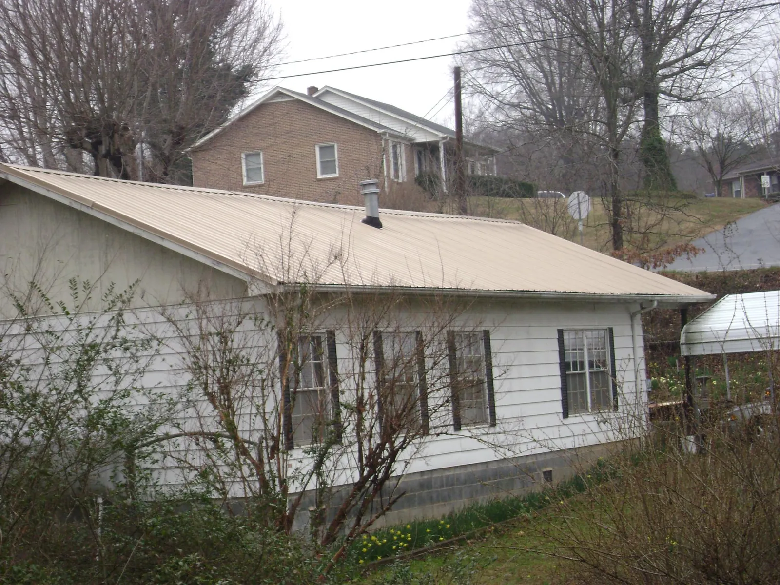 Tan metal roof on a white sided house set into a hillside — Commercial Roofing by Roofing Brothers in Ocoee